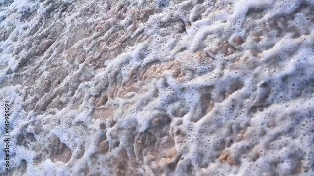 Close-up texture of the surface of a sea or ocean wave that comes to the sandy coast. Natural background with splashes of water and foam. Slow motion vacation summer concept Close-up texture of the surface of a sea or ocean wave that comes to the sandy coast. Natural background with splashes of water and foam. Slow motion vacation summer concept