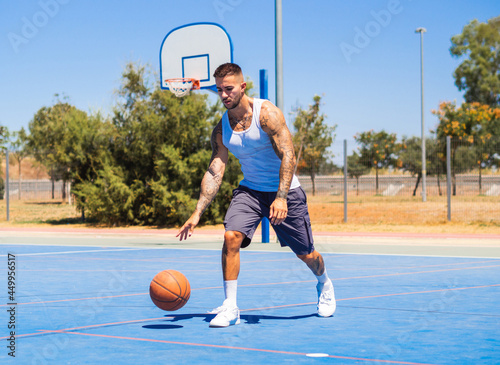 Hombre joven con tatuajes entrenando baloncesto en la calle
