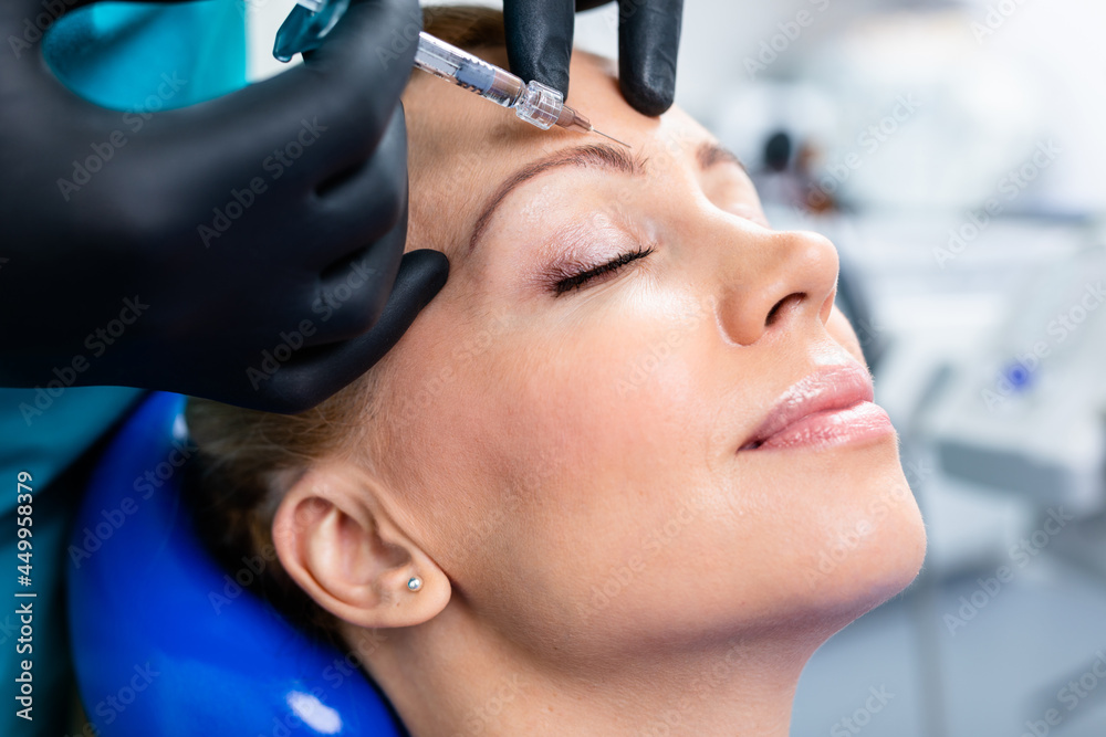 Naklejka premium Attractive woman is getting a rejuvenating facial injections. She is sitting calmly at clinic. The expert beautician is filling female wrinkles by hyaluronic acid.