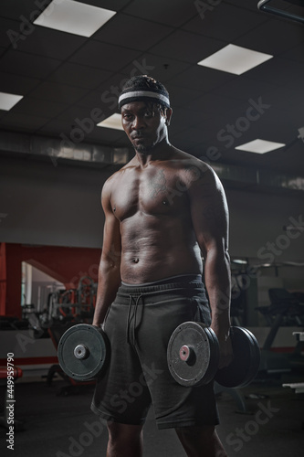 African american sports guy bodybuilder with naked muscular torso exercising with dumbbells in gym