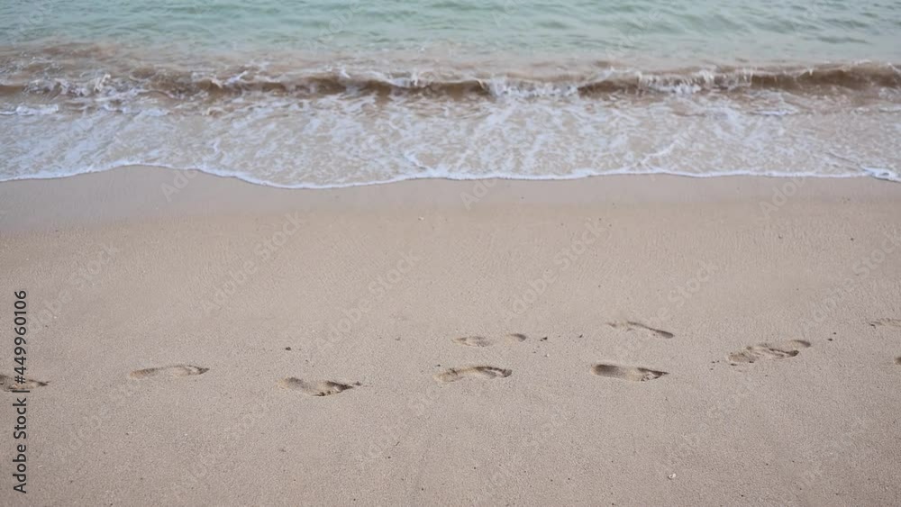 Close-up texture of the surface of a sea or ocean wave that comes washes away footprints in the sand coast. Natural background with splashes of water and foam. Slow motion vacation summer concept