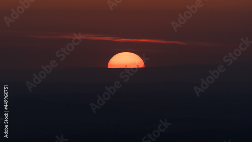 Sun setting over silhouetted hills with wind turbines