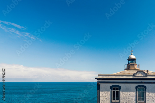 Minimalistic picture of the lighthouse located in Candás, municipality of Carreño, Principality of Asturias Spain. 
Fragment of a historic building above the blue calm sea and sky captured in summer. photo