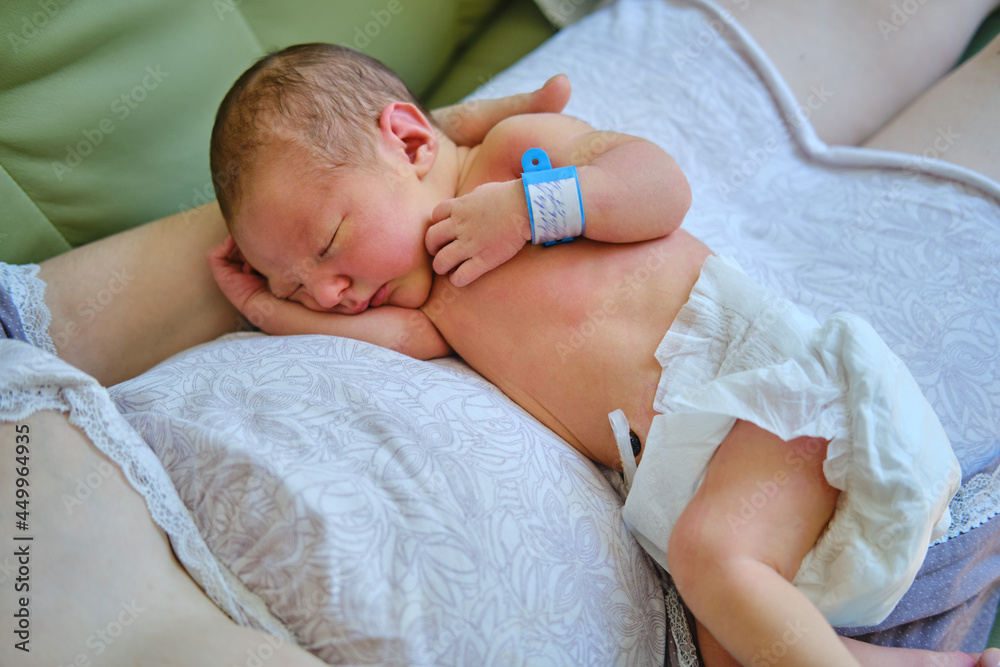 A mother is holding a newborn baby in her arms, with a maternity hospital bracelet on her arm. A newly born child in the clinic A mother is holding a newborn baby in her arms, with a maternity hospital bracelet on her arm. A newly born child in the clinic