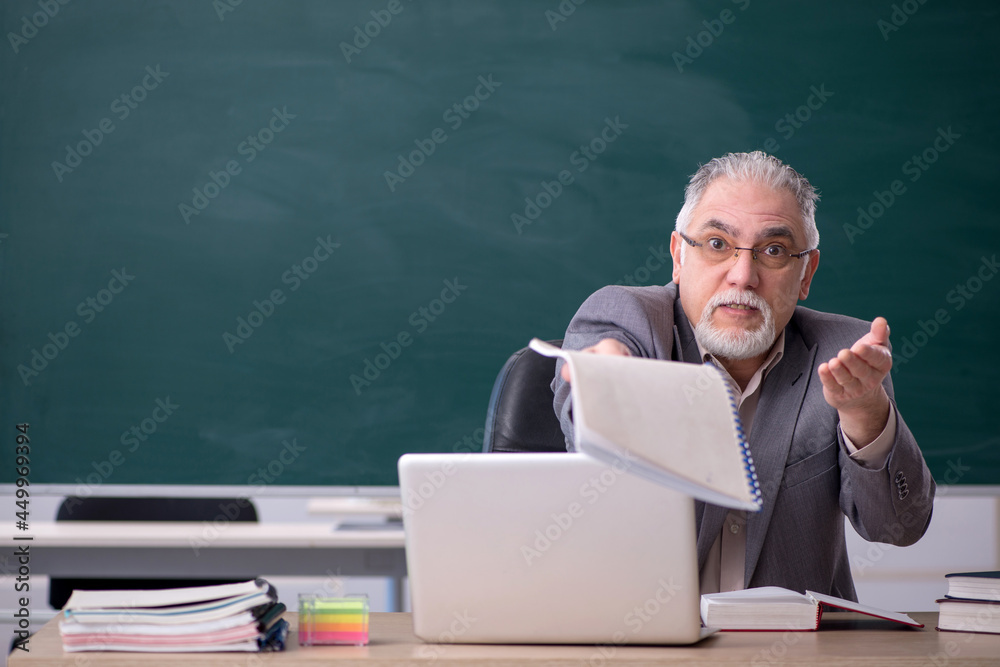 Old male teacher in front of blackboard Old male teacher in front of blackboard