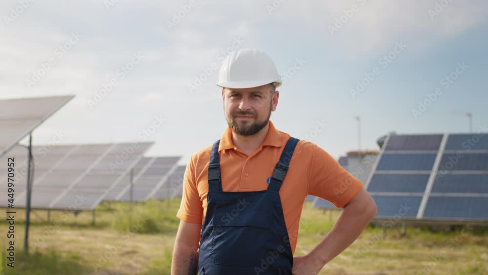Portrait of happy male engineer in protective helmet looking to camera. Handsome man in uniform smiling while standing at solar power farm. Concept of green energy. Industrial people. Energy Portrait of happy male engineer in protective helmet looking to camera. Handsome man in uniform smiling while standing at solar power farm. Concept of green energy. Industrial people. Energy