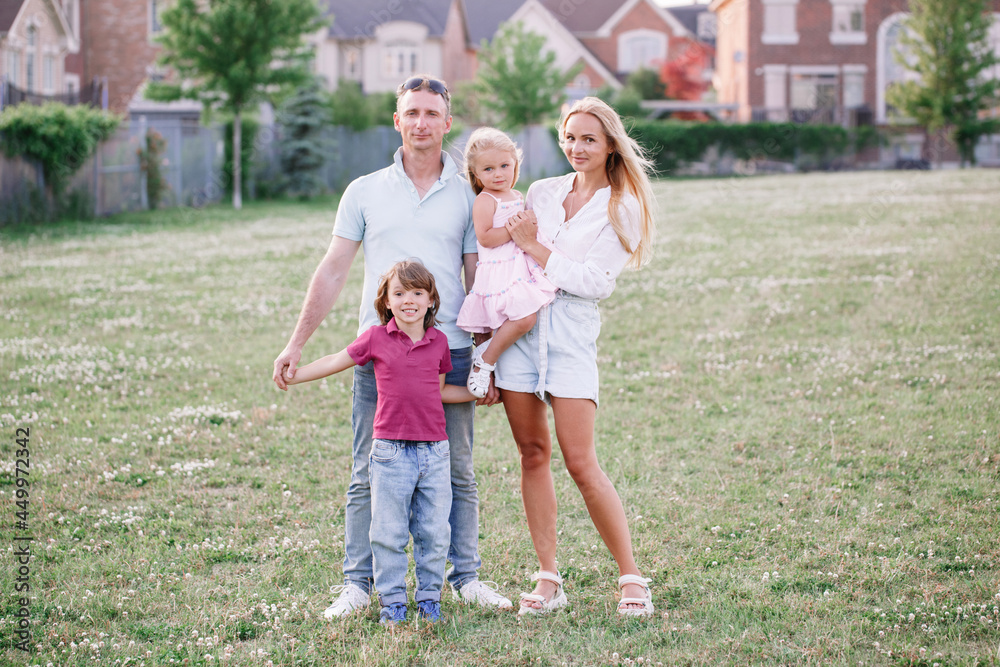 Happy Caucasian family with two kids boy and girl walking in park outdoor on summer day. Beautiful young family with daughter and son standing on meadow outside. Parents with children kids Happy Caucasian family with two kids boy and girl walking in park outdoor on summer day. Beautiful young family with daughter and son standing on meadow outside. Parents with children kids