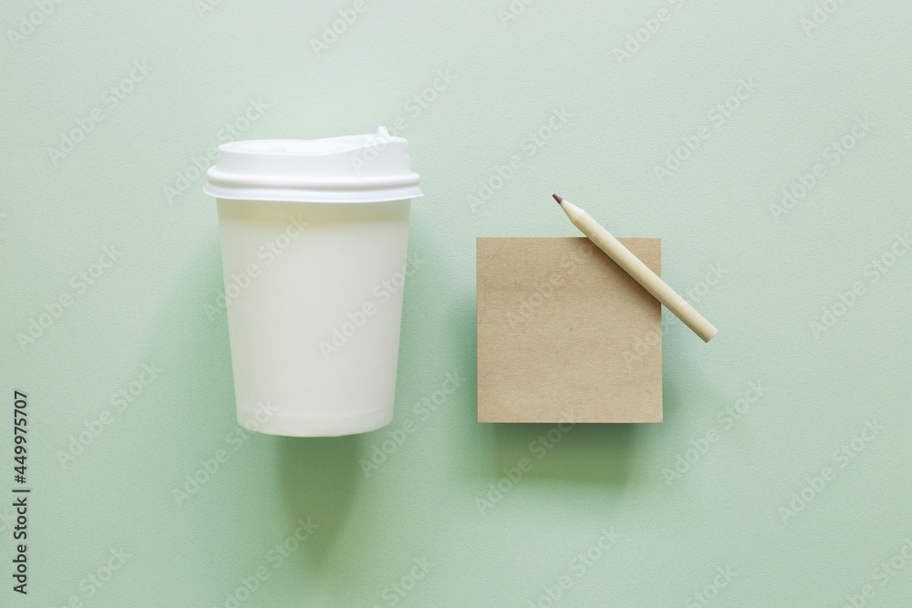 Brown kraft memo pad, pencil, paper coffee cup on green background. top view, copy space Brown kraft memo pad, pencil, paper coffee cup on green background. top view, copy space