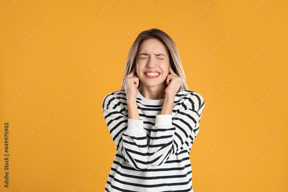 Emotional young woman covering her ears with fingers on yellow background Emotional young woman covering her ears with fingers on yellow background