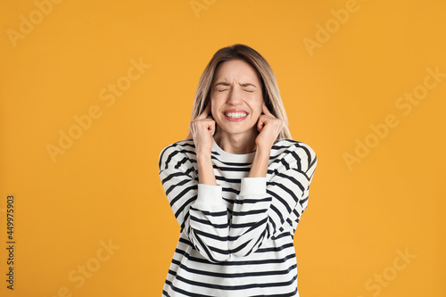 Emotional young woman covering her ears with fingers on yellow background © New Africa