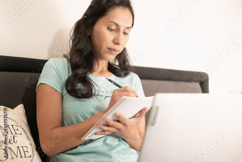 Woman working in home office from bed using cell phone and laptop and back massager