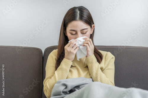 Sick, Coronavirus covid-19 asian young woman, girl headache under blanket have a fever, flu and use tissues paper sneezing nose, runny sitting on sofa bed at home. Health care on virus person..