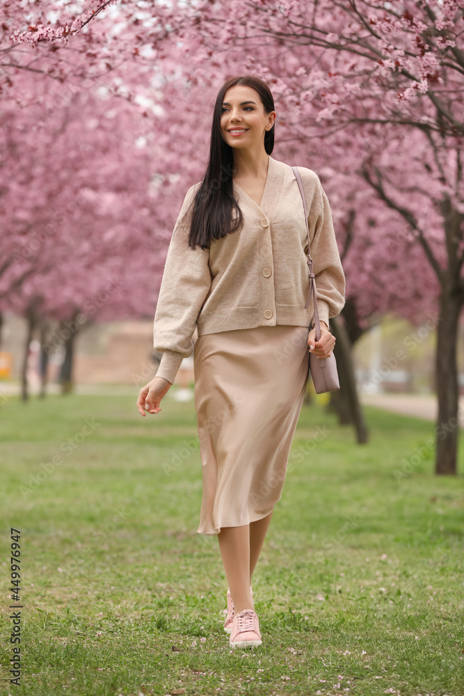 Pretty young woman in park with blooming trees. Spring look Pretty young woman in park with blooming trees. Spring look