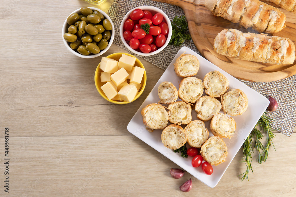 Garlic bread in white square plate on the table with cheese, rosemary, olives and cherry tomatoes. Top view. Garlic bread in white square plate on the table with cheese, rosemary, olives and cherry tomatoes. Top view.