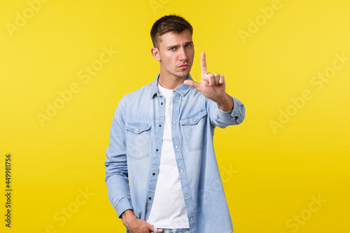 Lifestyle, people emotions and summer leisure concept. Serious-looking displeased blond man shaking finger as scolding person, give warning or prohibit bad action, disagree over yellow background photo