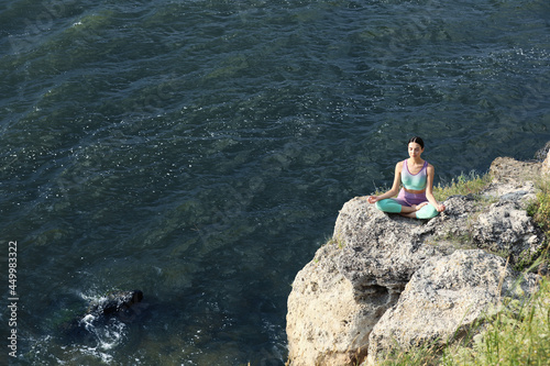 Young woman meditating on cliff near river. Space for text