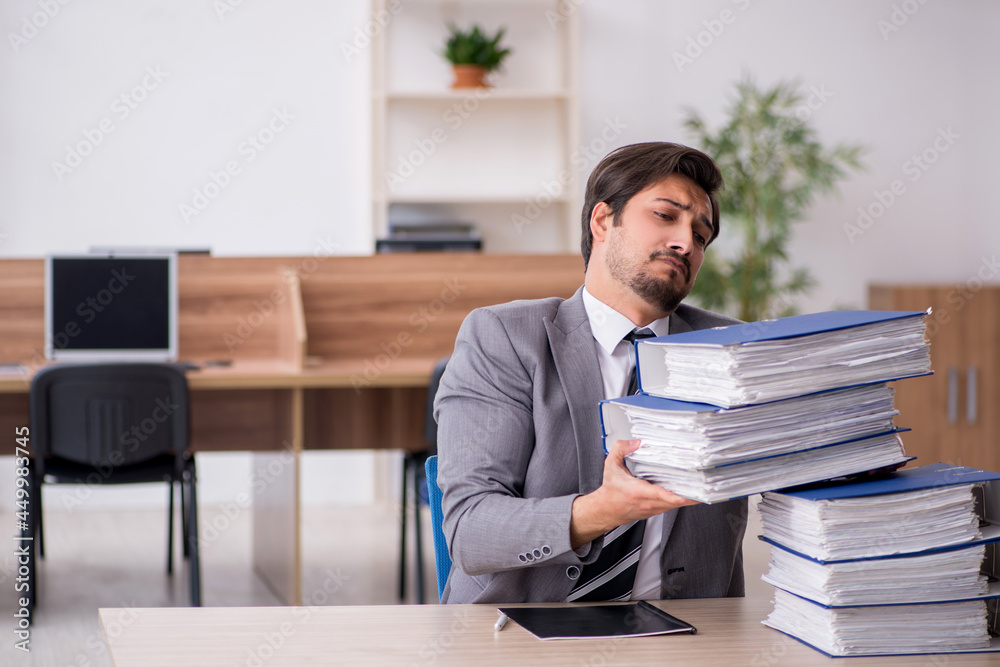 Young male employee unhappy with excessive work in the office Young male employee unhappy with excessive work in the office