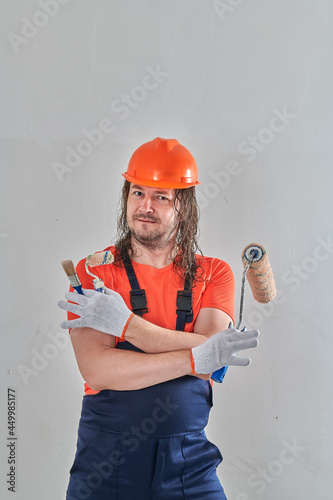 a builder stands in overalls with a roller and a brush