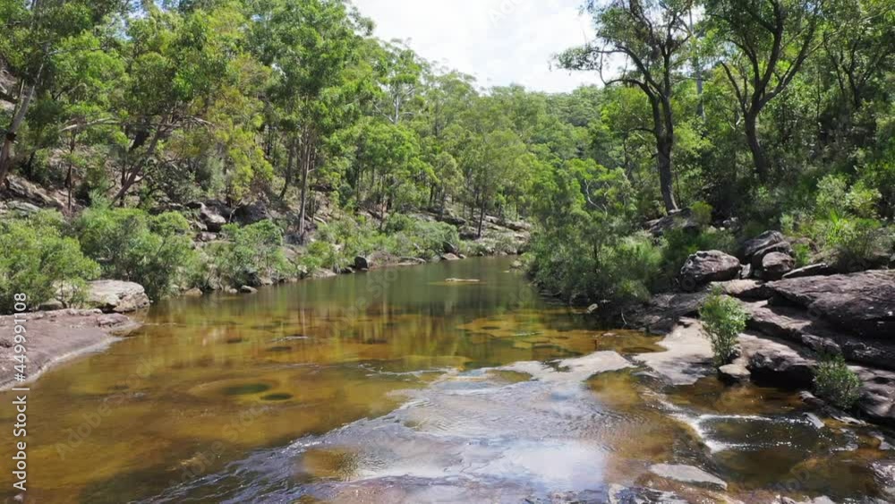 Drone aerial flyover of a wide river to reveal waterfall into large water basin on a sunny day near the Georges River, Sydney - Australia Drone aerial flyover of a wide river to reveal waterfall into large water basin on a sunny day near the Georges River, Sydney - Australia