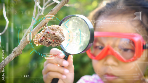 Asian little girl examining wasp's nest through a magnifying glasswith digitally generated holographic display tech data visualization. Concept of self learning trips lifestyle in springtime.