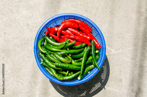 green chilis and red chilis in a blue plastic basket on a concrette. photo