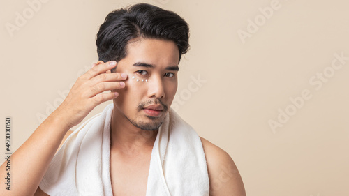 Men's skin care. Asian men with mustaches apply eye cream to reduce dark circles on brown background. Young man facial face care.