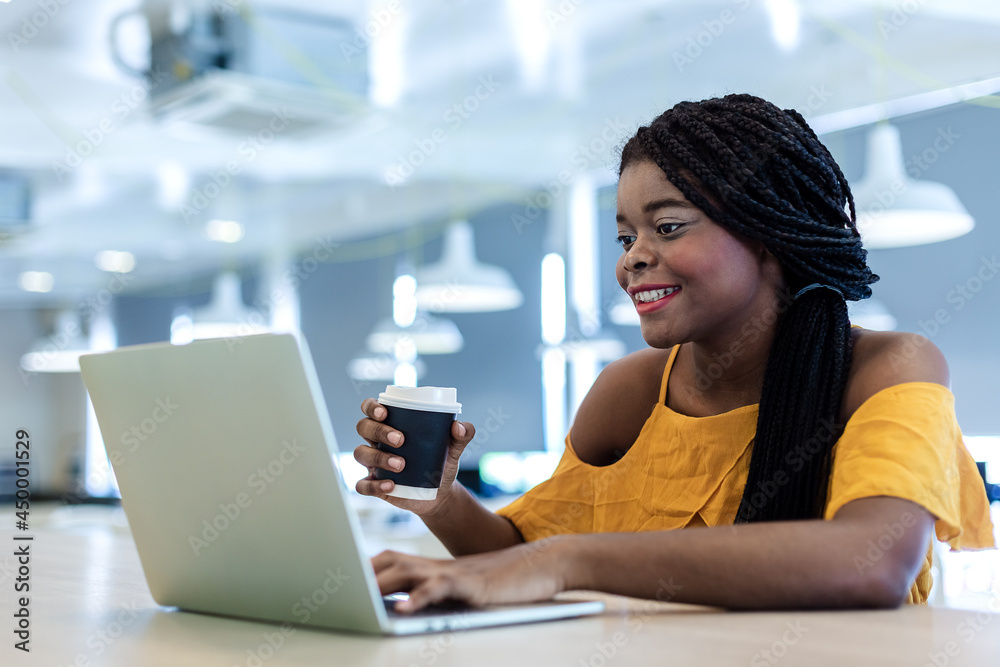 happy young businesswoman African American cheerful demeanor raise holding coffee cup smiling looking laptop screen. female working successful.