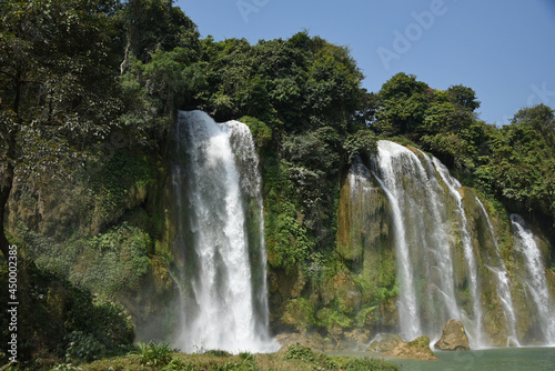 Big waterfall Ban Gioc among trees and mountains on a sunny summer day