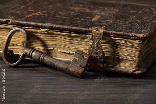 Door, old, metal key next to an antique book on clasps. Retro items on a dark table, studio shot.
