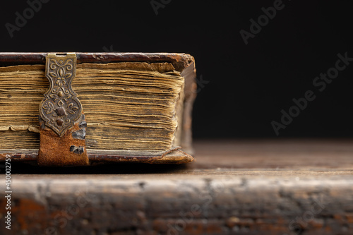 Part of an antique book on a clasp is visible on an old wooden table, close-up. photo