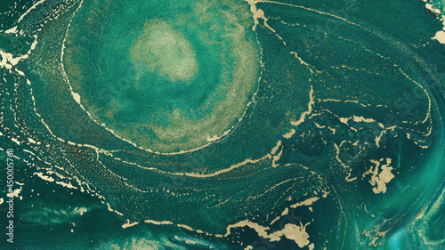 Abstract explosion of green paints gold sparkles close-up. Hypnotic current liquid ink. Emerald color of spreading, moving mesmerizing background. Texture of golden threads on green tide