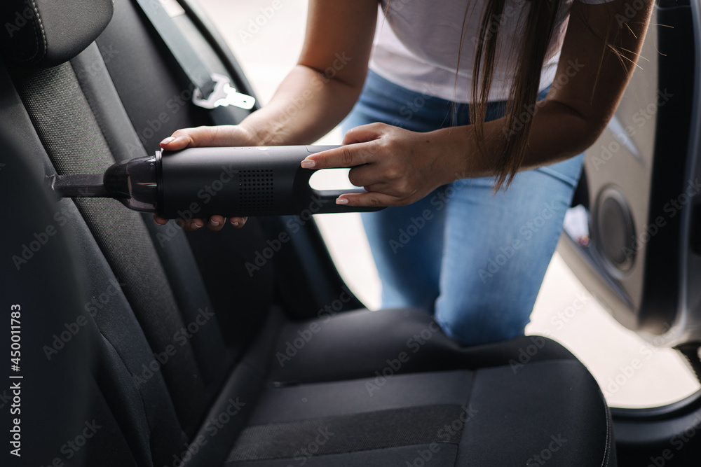 Close-up of female using portable vacuum cleaner in her car. Car interior cleaning. Woman vacuuming seats. Dust and dirt removal