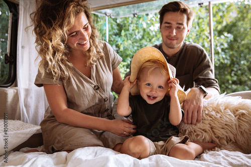 Loving parents enjoy spending time with little kid boy travelling together on camper rv. Happy young family on road trip vacation: caring mom and dad bonding cuddle with small child in caravan trailer photo