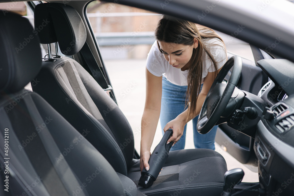 Woman vacuuming her car in the garage at home. Female using portable vacuum cleaner to remove dust and dirt. Car interior cleaning