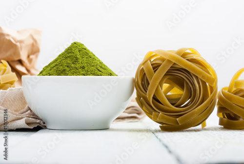 uncooked taglatelle pasta and ingredients: grounded spinach powder and whole wheat flour photo