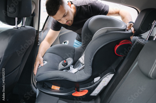 Man installs a child car seat in car at the back seat. Responsible father thought about the safety of his child