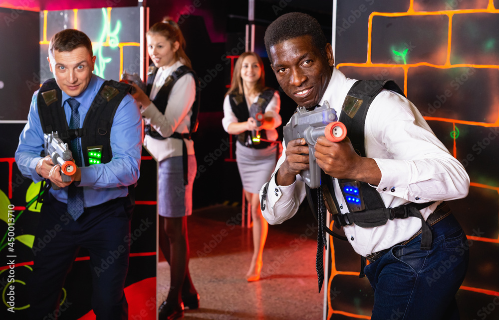 Satisfied pleasant positive men and women in business suits playing laser tag emotionally in dark room