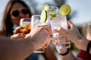 Group of young people clinking cocktail drink glasses toasting. Best friends wearing a lowered face mask having a funny reunion.