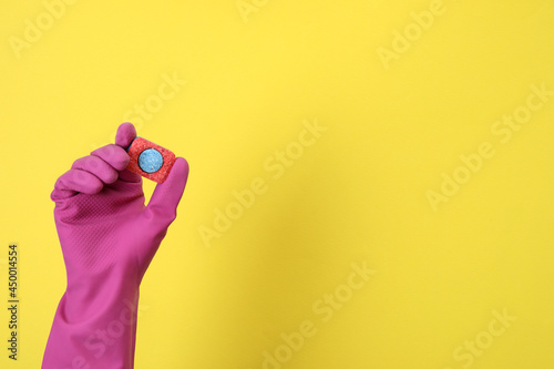 Hand in glove holds dishwashing tablet on yellow background