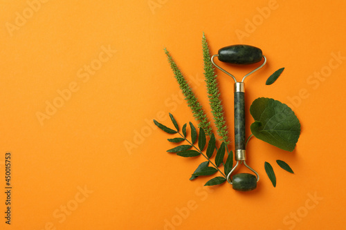 Fotografie Green face roller and leaves on orange background