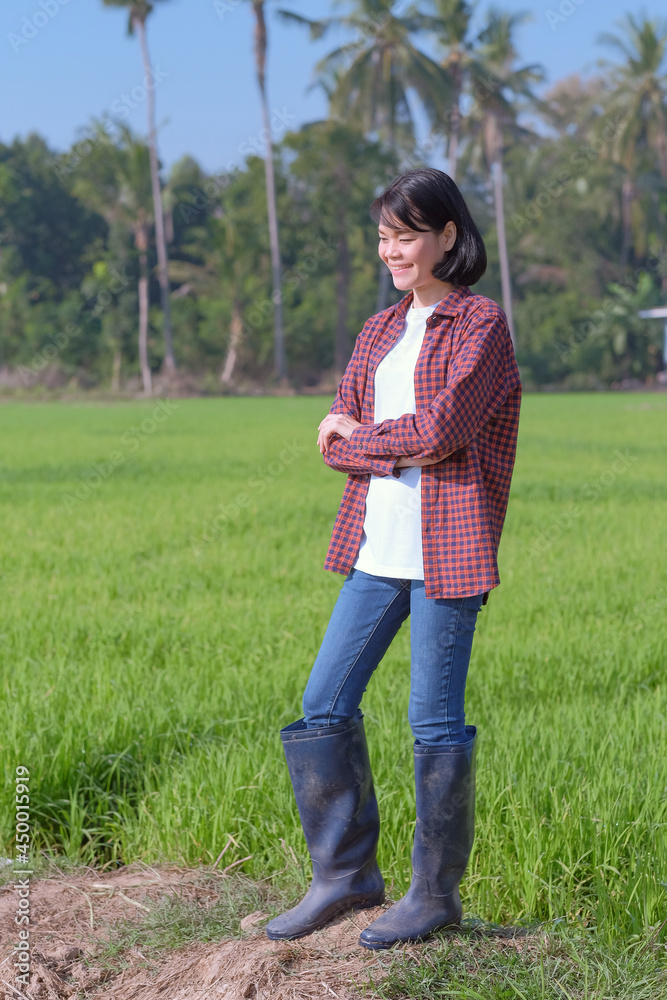 A farmer woman in a striped shirt is smiling at a green field.