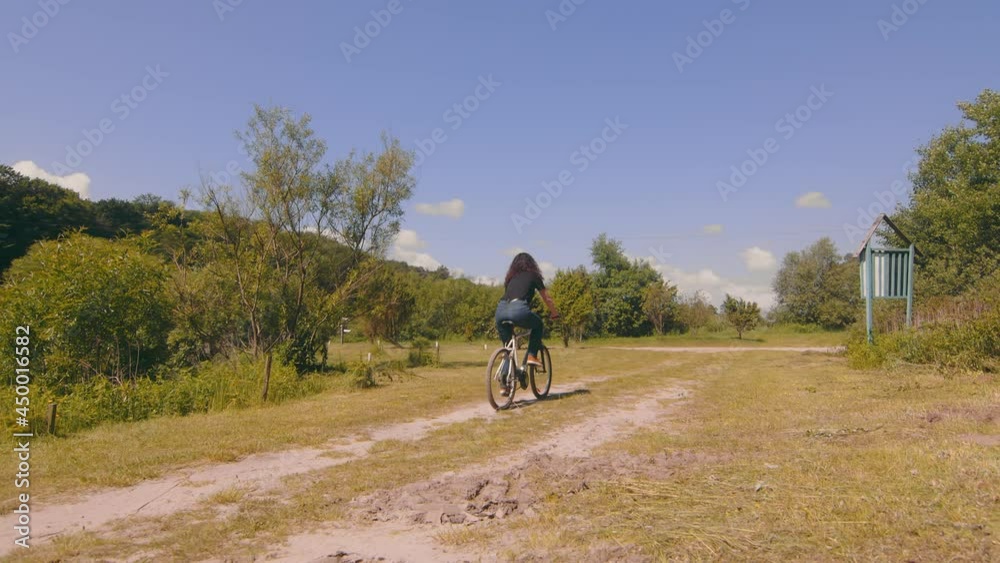 View from the back of a girl riding a bike on the road. Cycling on a field road. Young woman pedals a bicycle View from the back of a girl riding a bike on the road. Cycling on a field road. Young woman pedals a bicycle
