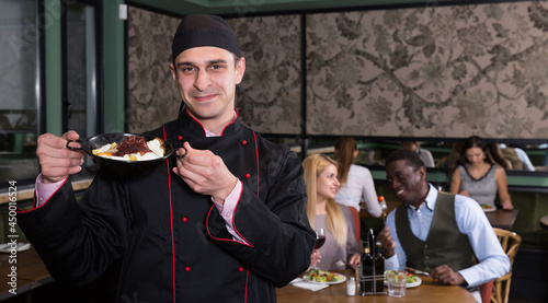 Portrait of confident chef standing with cooked dish in restaurant hall