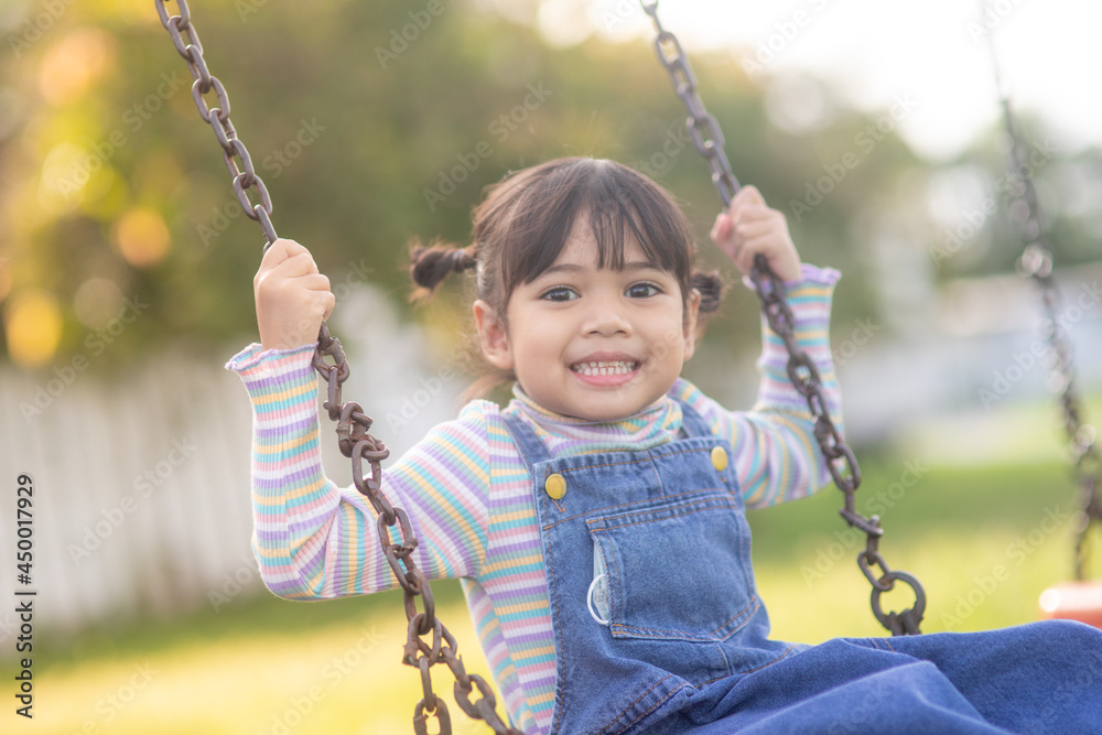 Happy little Asian girl playing swing outdoor in the park