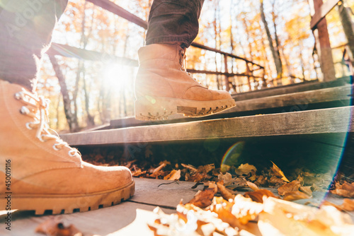 Woman hiker goes up metal stairs in picturesque autumn park with colorful trees back low angle shot