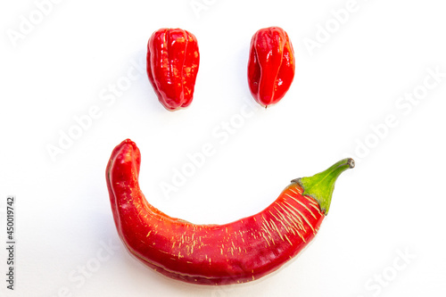 Cheerful smile from Habanero and Rezha peppers. Facial image made of hot red pepper isolated on white background. Friendly vegetable food concept