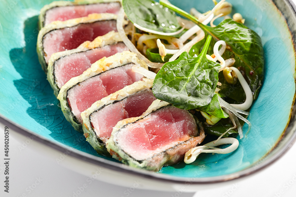 Tuna tataki - seared tuna,. thinly sliced sashimi style. Tuna tataki served with delicious citrus ponzu tataki sauce. Japanese seafood on black plate isolated on white background.