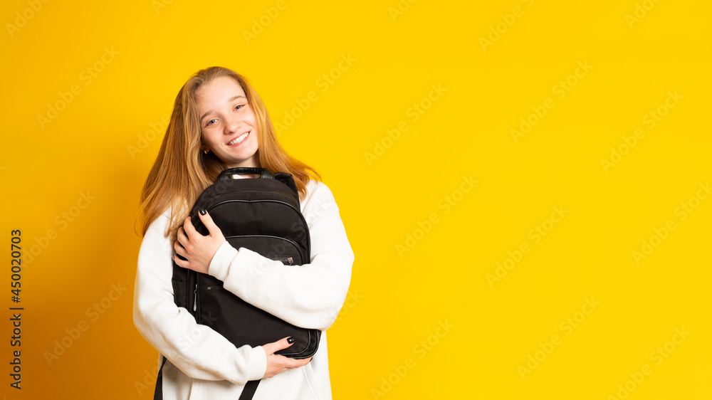 Banner copy space. Smiling young girl dressed white hoodie on yellow background with backpack. Positive cool schoolgirl with backpack. Banner copy space. Smiling young girl dressed white hoodie on yellow background with backpack. Positive cool schoolgirl with backpack.