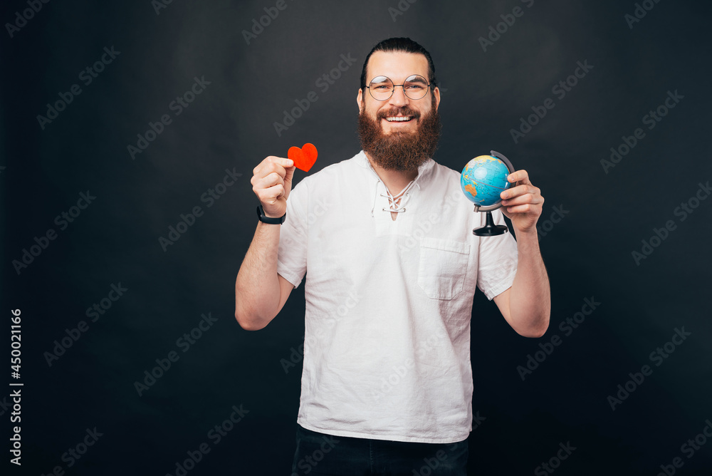 I love to travel, cheerful young man with beard holding globe and red paper heart I love to travel, cheerful young man with beard holding globe and red paper heart