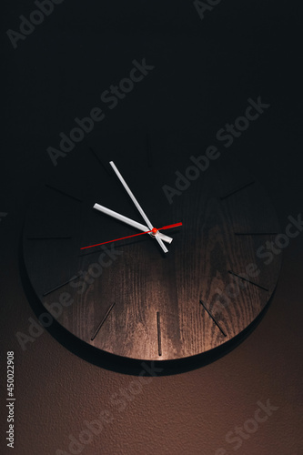 Wooden minimalistic clock hanging on a black wall